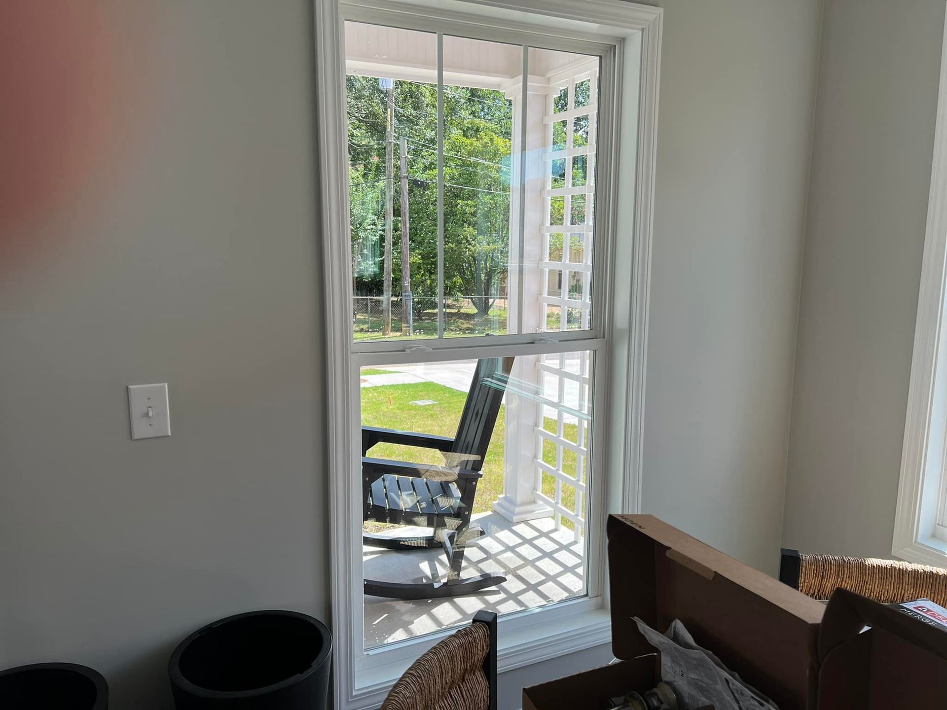 A rocking chair is sitting on a porch next to a window.