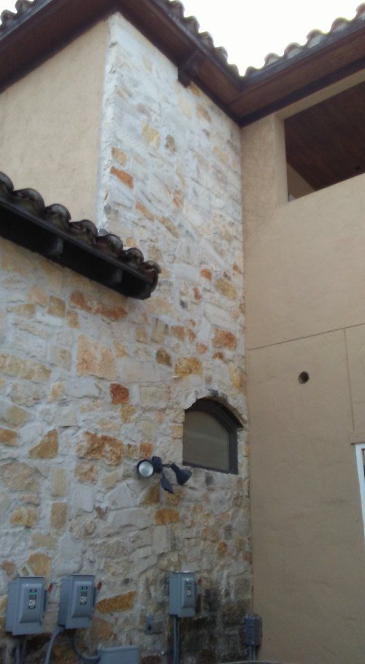 Exterior of a building with stone and stucco walls, a brown tiled roof, and an arched window.