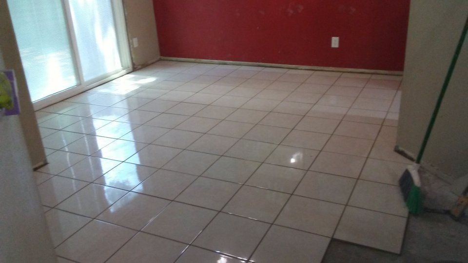 White tiled floor reflecting light in a room with red wall and sliding glass door.