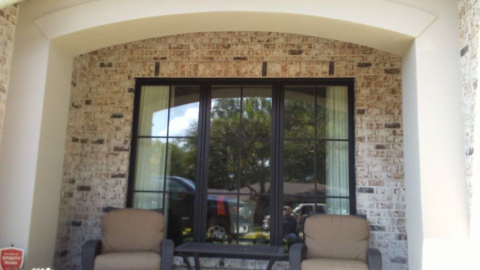 Covered porch with brick wall, black framed window, chairs, and table.