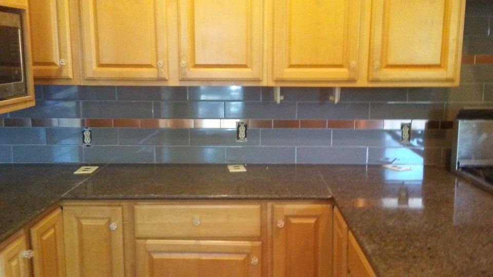 Kitchen with brown cabinets, gray tile backsplash, copper accents, and dark countertops.