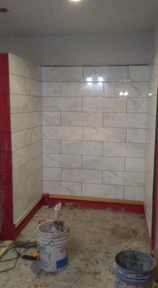 Bathroom under construction with white tiled walls and red waterproofing. Buckets and tools on the floor.