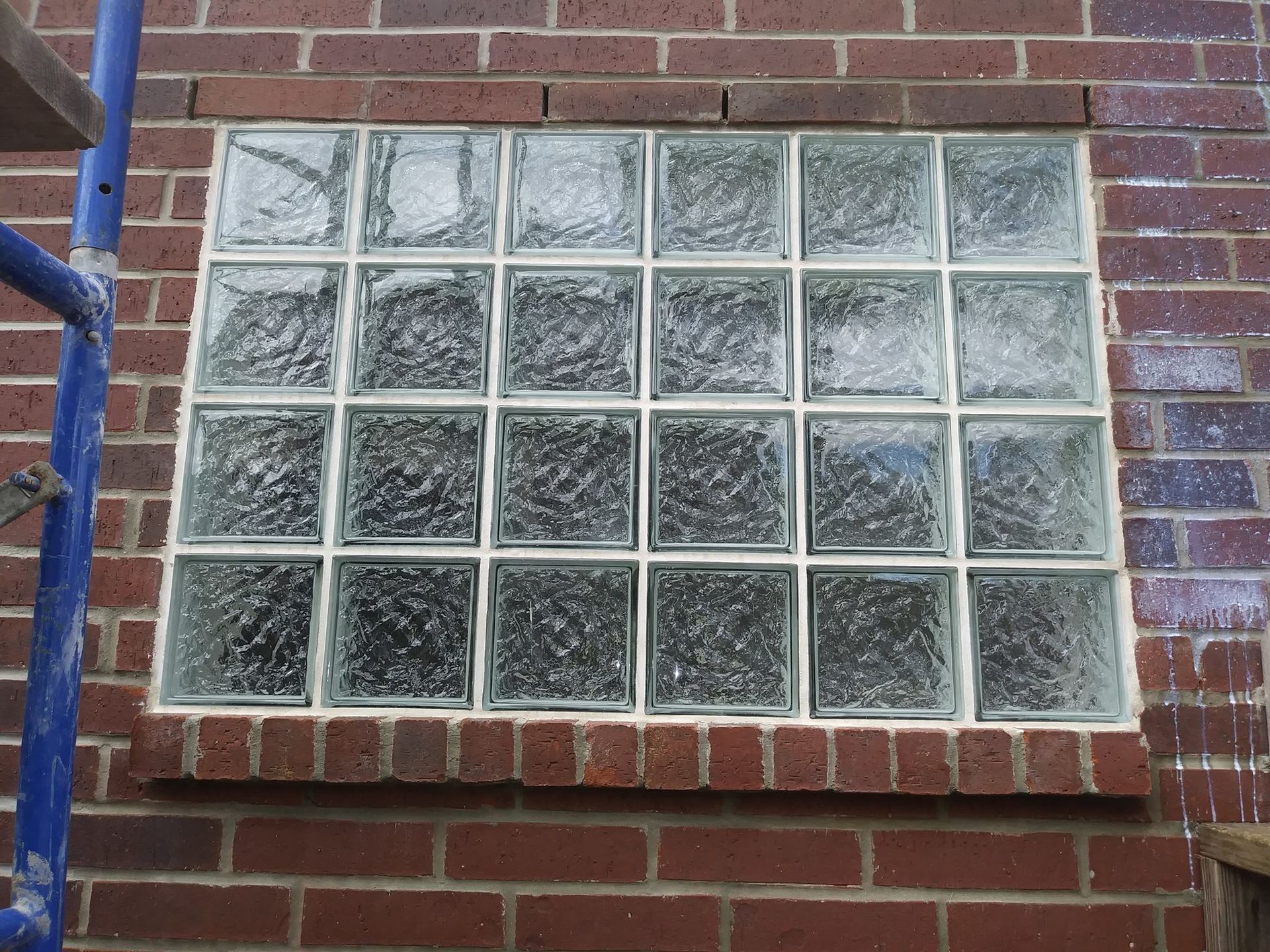 Glass block window set in a red brick wall. Blue scaffolding is visible to the left.