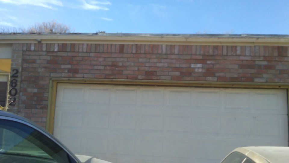 Garage door beneath brick facade, car visible in foreground, blue sky above.
