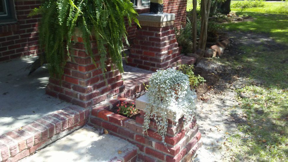 Brick porch with potted ferns and hanging greenery; front yard with grass.
