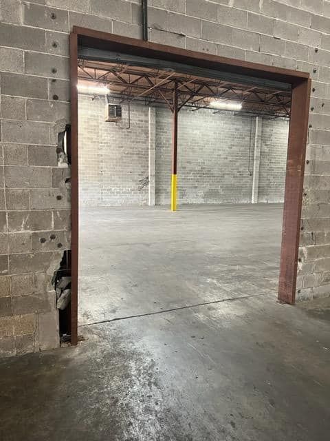 Open doorway into a large, empty warehouse with concrete block walls and floor, and steel beams.
