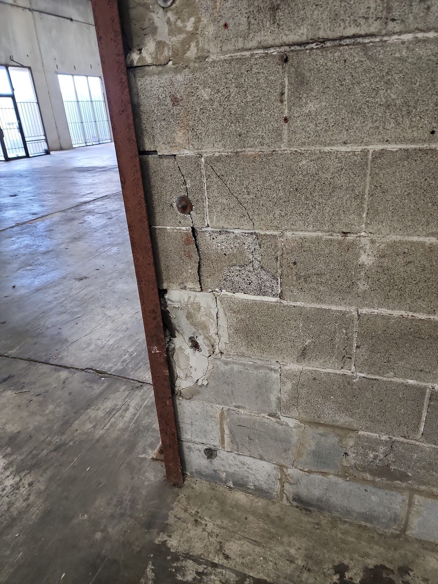 Concrete block wall with vertical crack and rusty metal beam. Industrial setting.