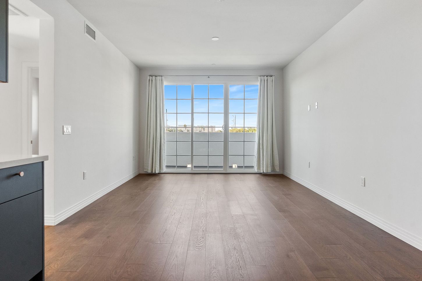 An empty living room with hardwood floors and a balcony.