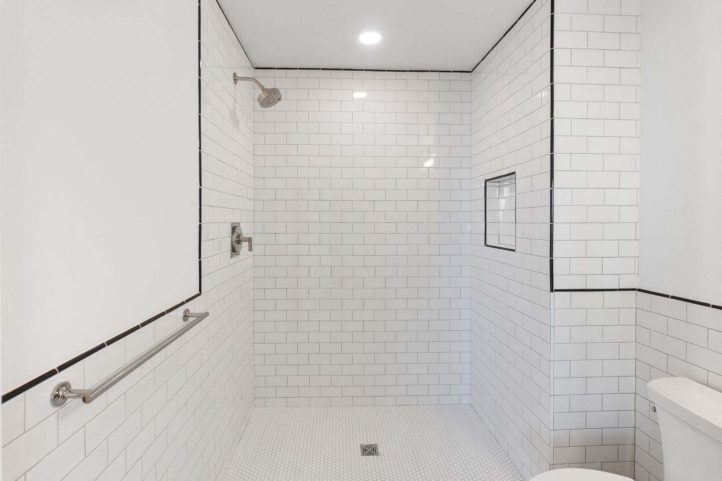 A bathroom with white tiles , a toilet , and a walk in shower.