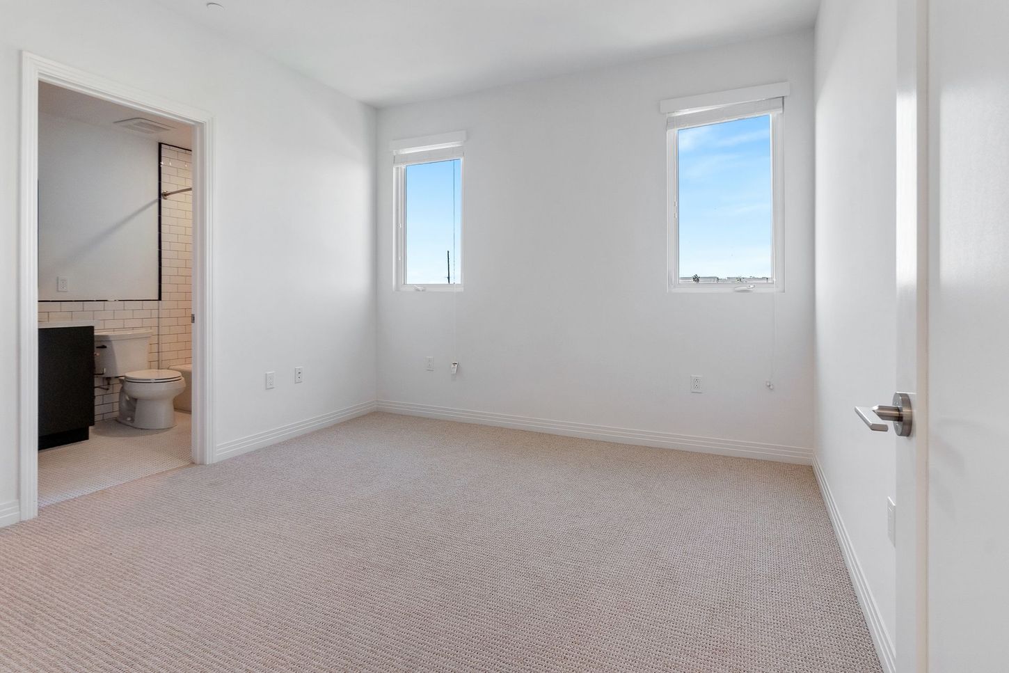 An empty bedroom with two windows and a toilet.