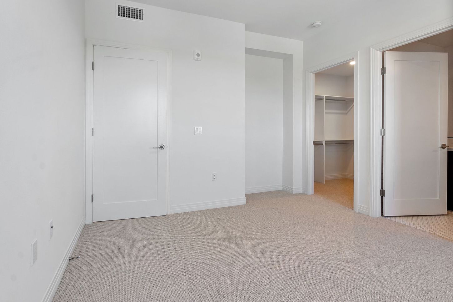 An empty bedroom with a walk in closet and a carpeted floor.