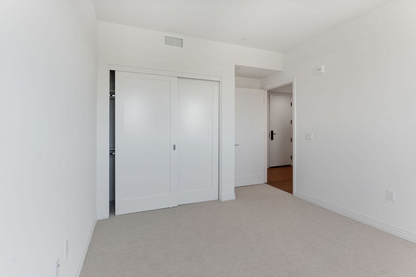 An empty bedroom with white walls and a carpeted floor.