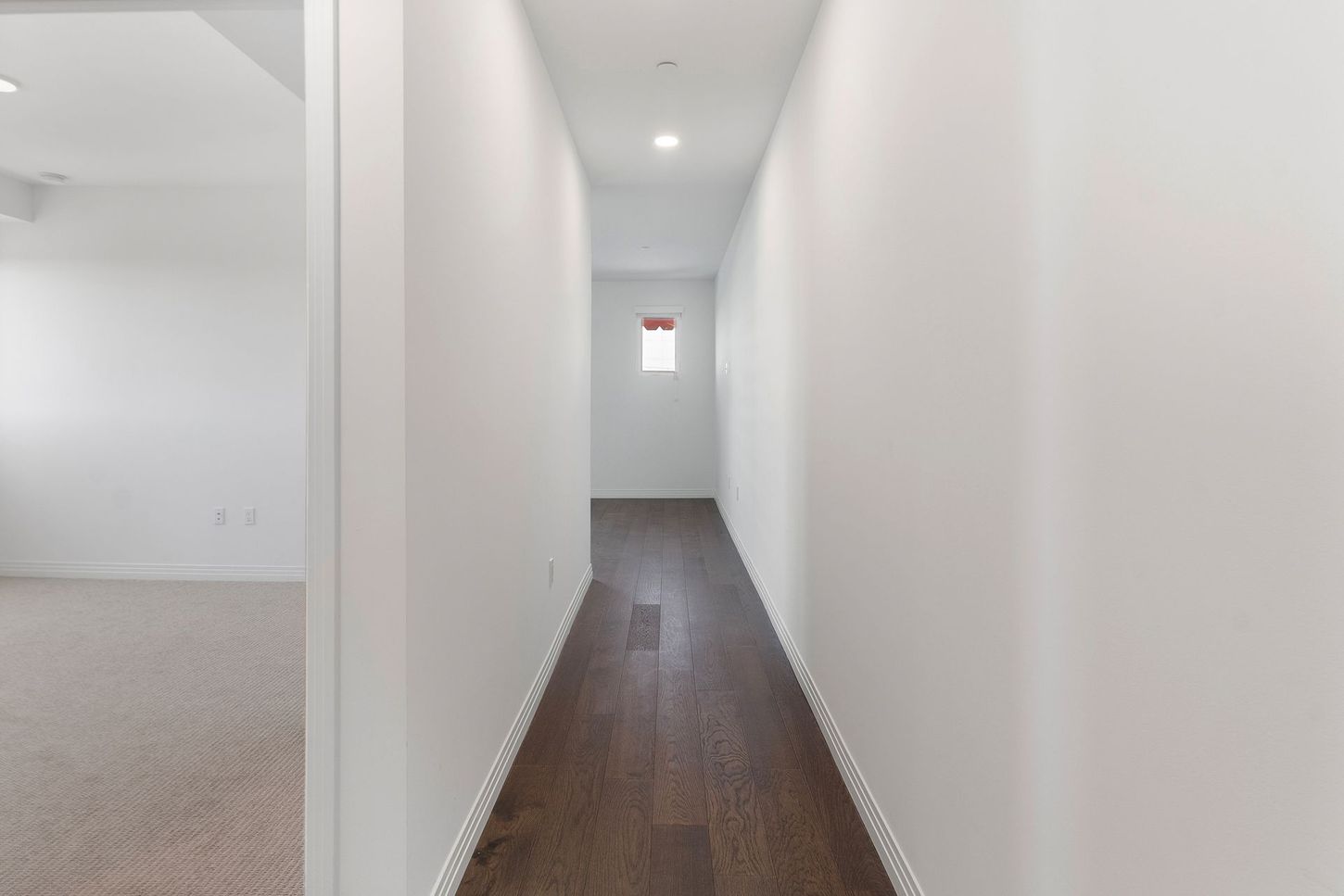 A long hallway with hardwood floors and white walls in a house.