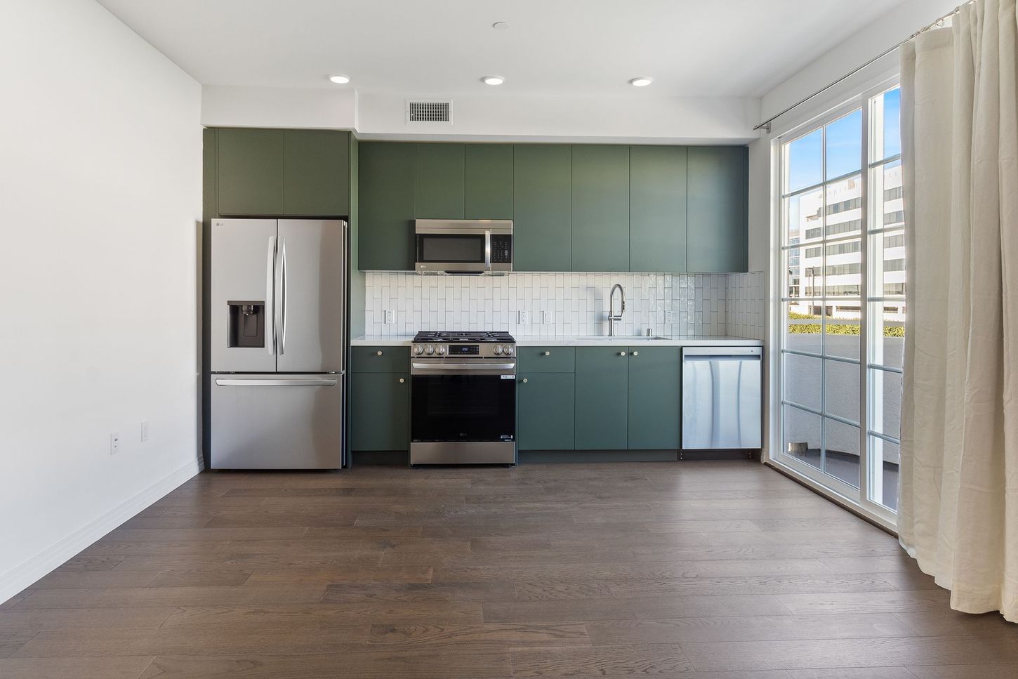 An empty kitchen with green cabinets and stainless steel appliances