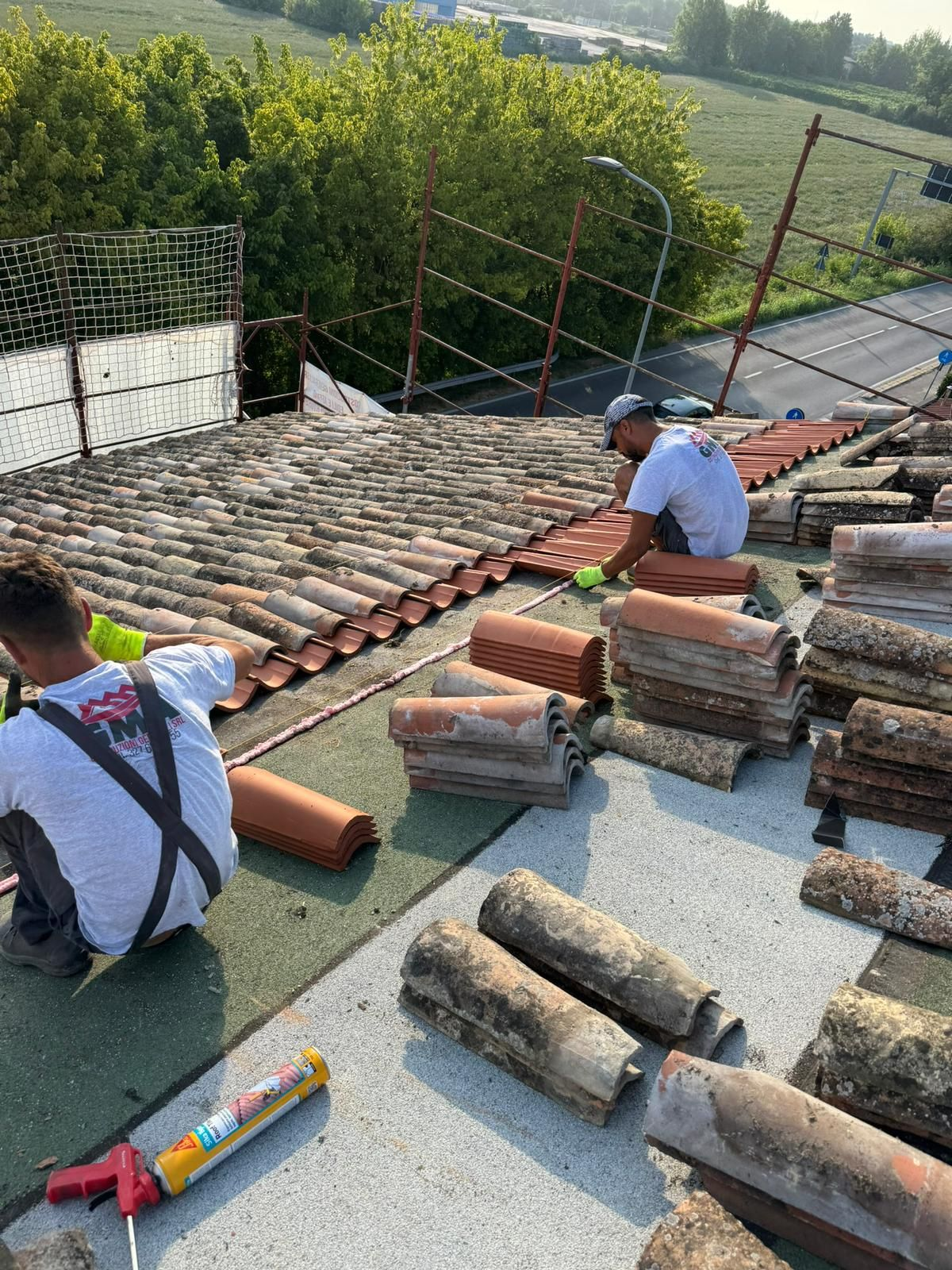 Un tetto parzialmente in costruzione, con listelli di legno, sezioni a vista e una pila di tegole rosse.