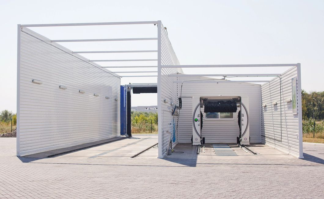 Una struttura esterna per il lavaggio automatico delle auto, con pareti a doghe bianche e un'unità di lavaggio robotizzata al centro.