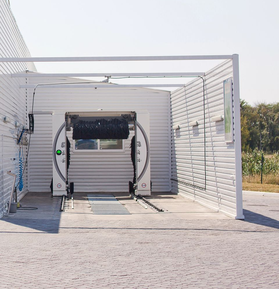 Una postazione di autolavaggio drive-through con struttura bianca e meccanismo automatico di spazzolatura all'interno.