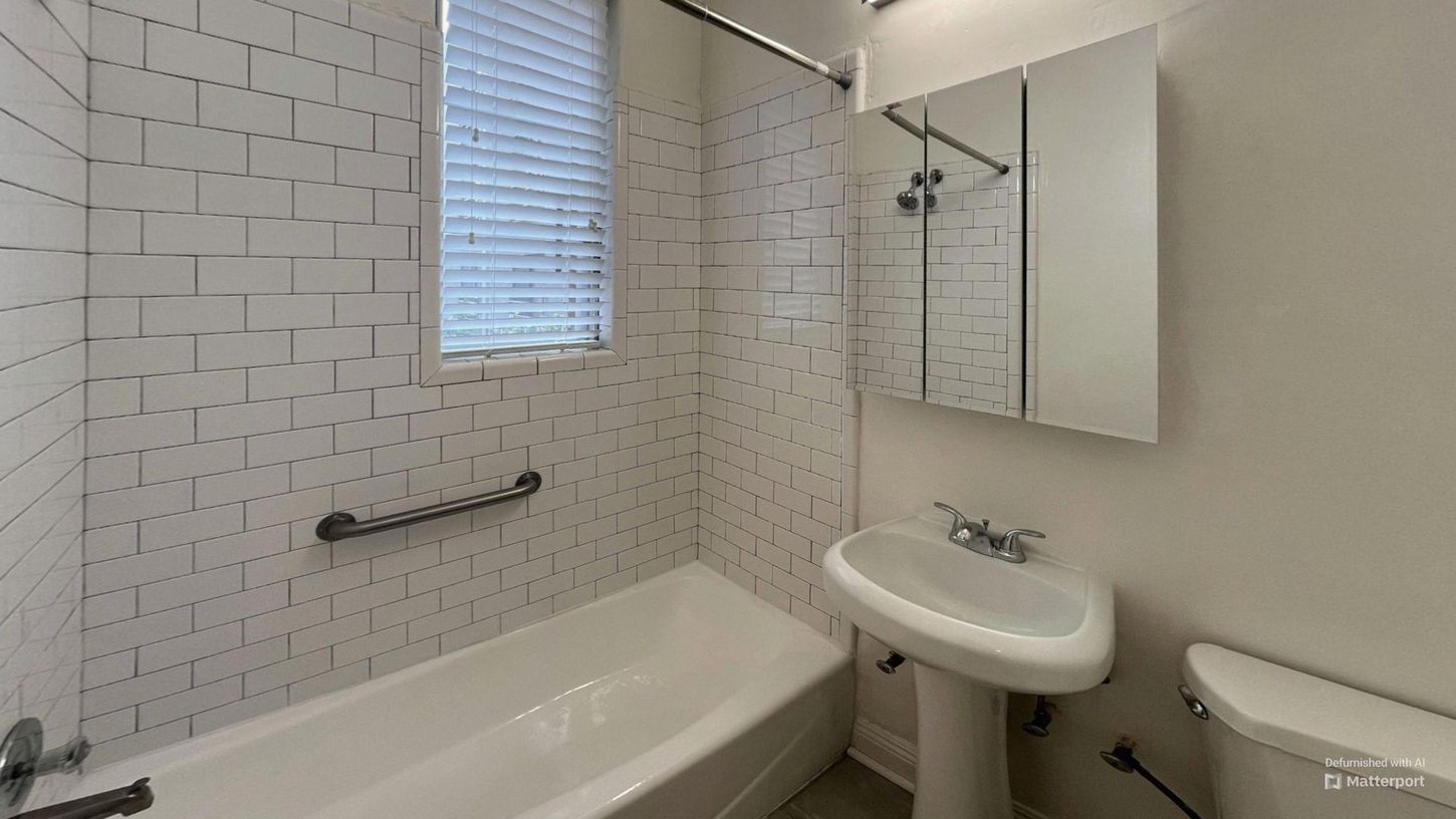 Small bathroom with white subway tile, a bathtub, pedestal sink, and a window with blinds.