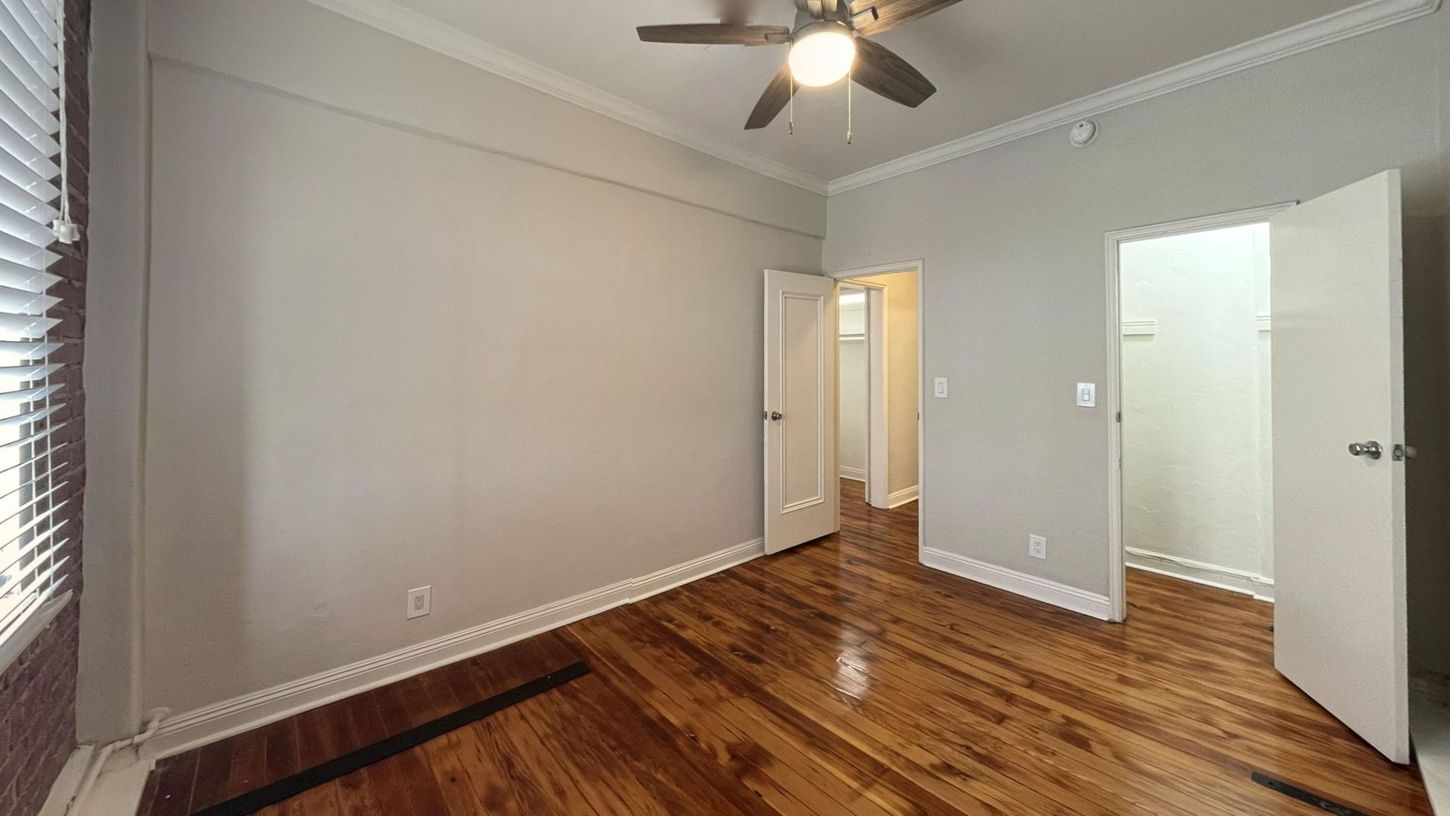 Empty bedroom with wood floor, white trim, grey walls, and open doors to closet and hallway.