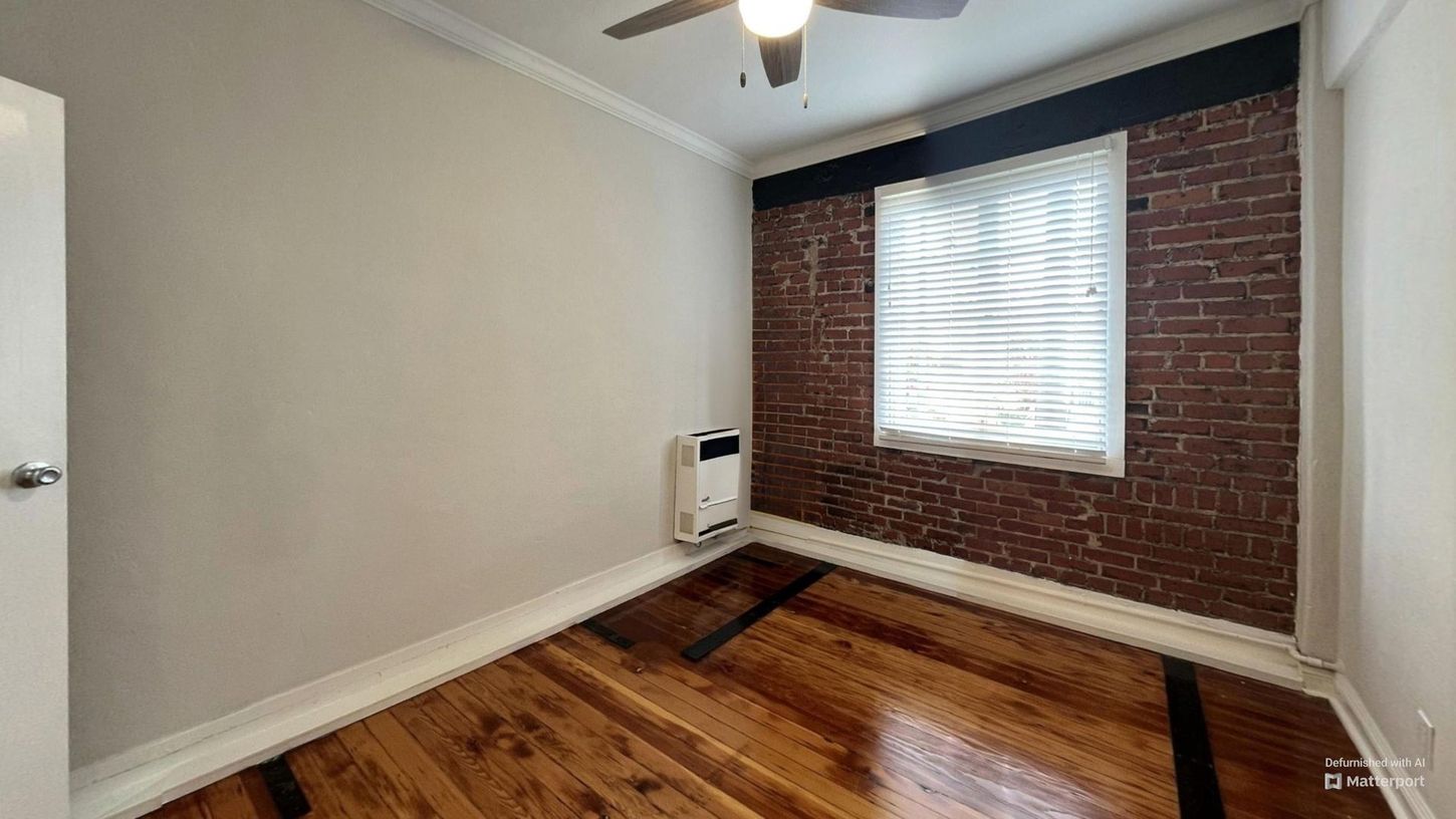 Empty room with brick accent wall and hardwood floors.