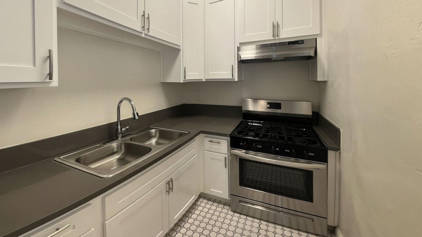 Small white kitchen with stainless steel appliances, dark countertops, and tile flooring.