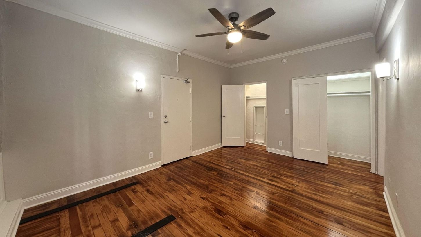 Empty bedroom with hardwood floors, white doors, and a ceiling fan.