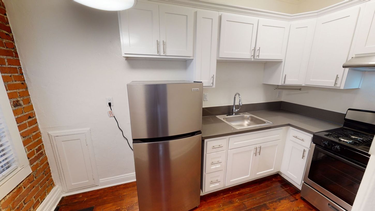 Kitchen with stainless steel refrigerator, white cabinets, and gas stove in a small space.