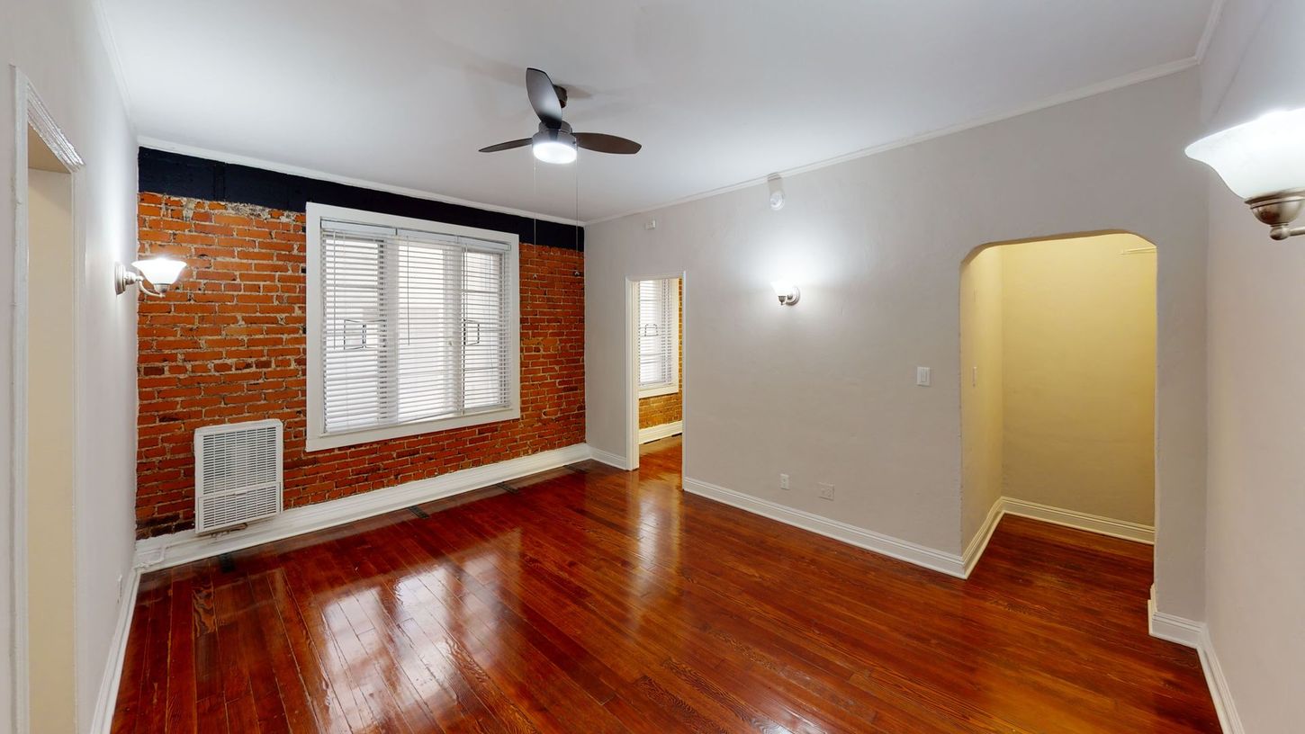 Interior of a room with exposed brick wall, hardwood floors, and a ceiling fan.