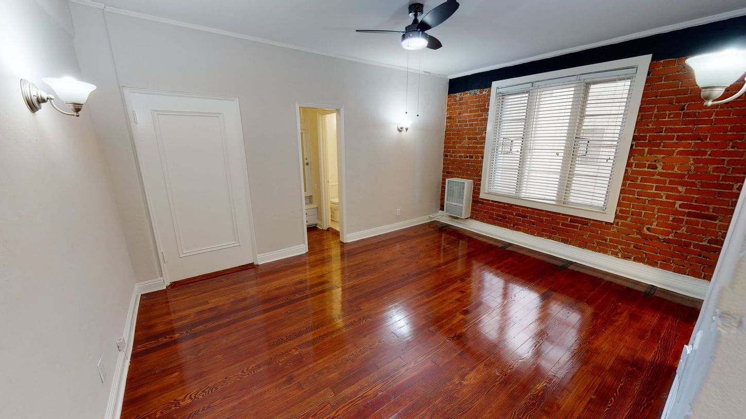 Empty room with wood floors, brick accent wall, and a window.