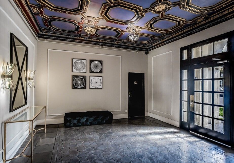 Elegant foyer with ornate ceiling, artwork, dark bench, and black door.