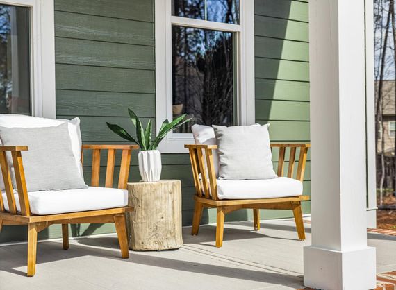 There are two chairs and a table on the porch of a house.