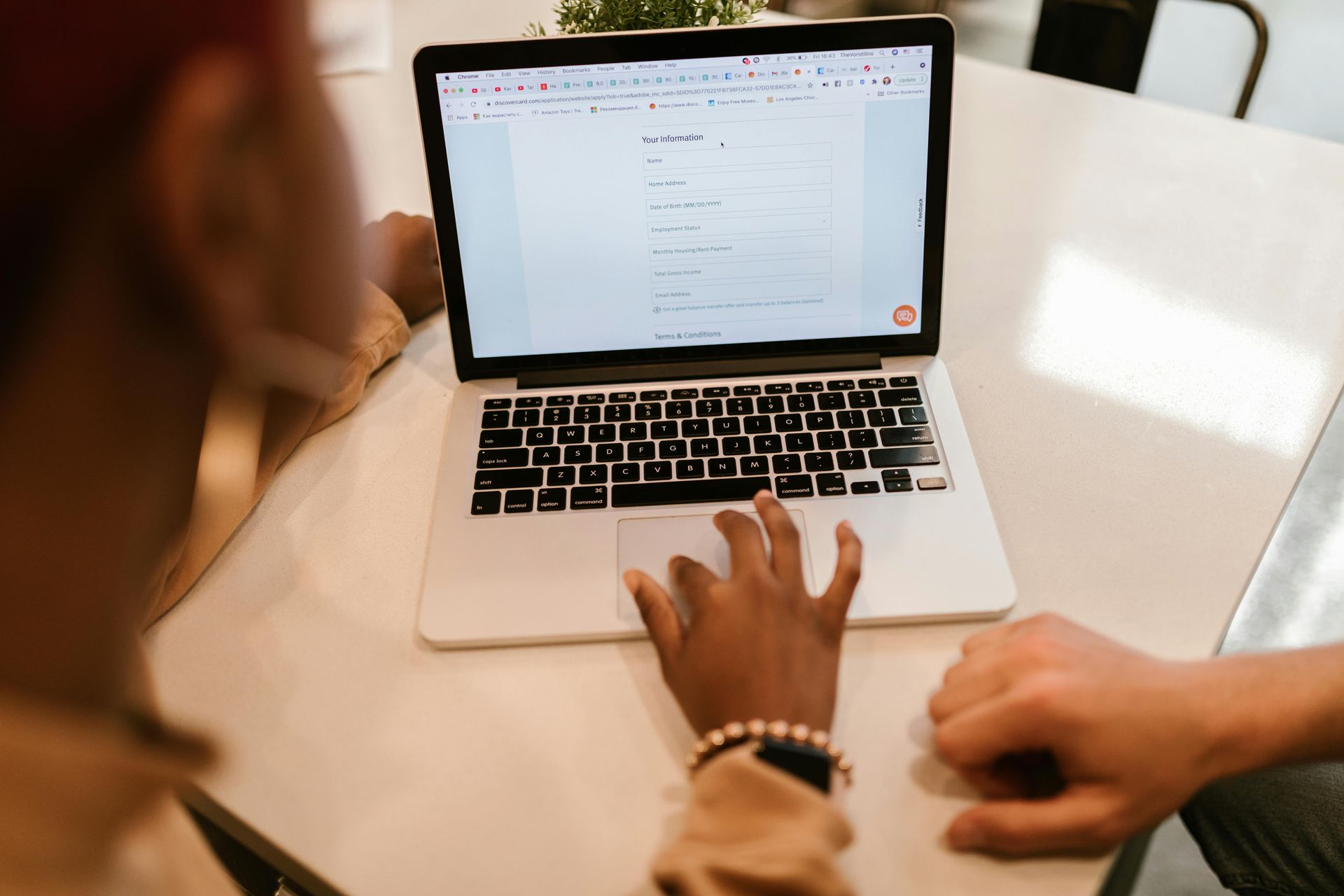 Person using a laptop at a white table, with another person's hand visible.