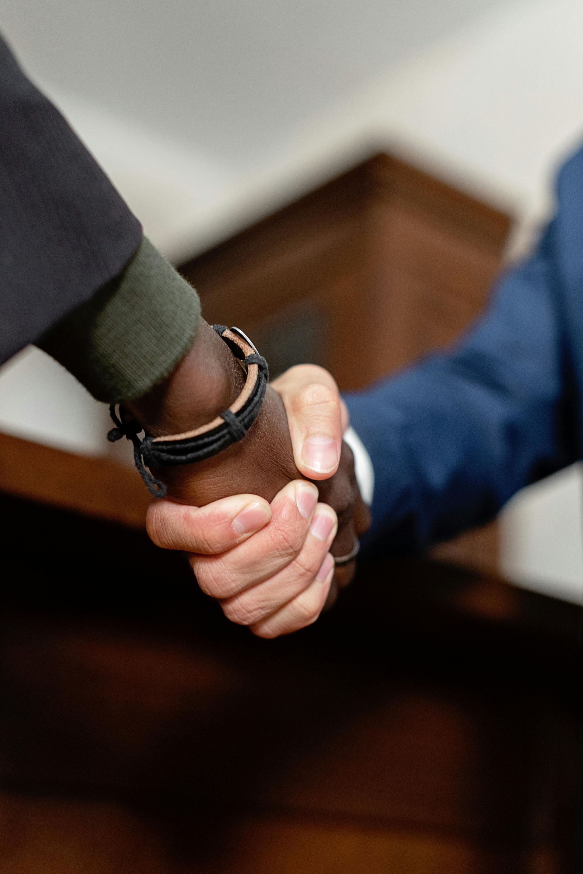 Two men shaking hands, one with dark skin, the other with light skin. They are in a room with dark wood paneling.