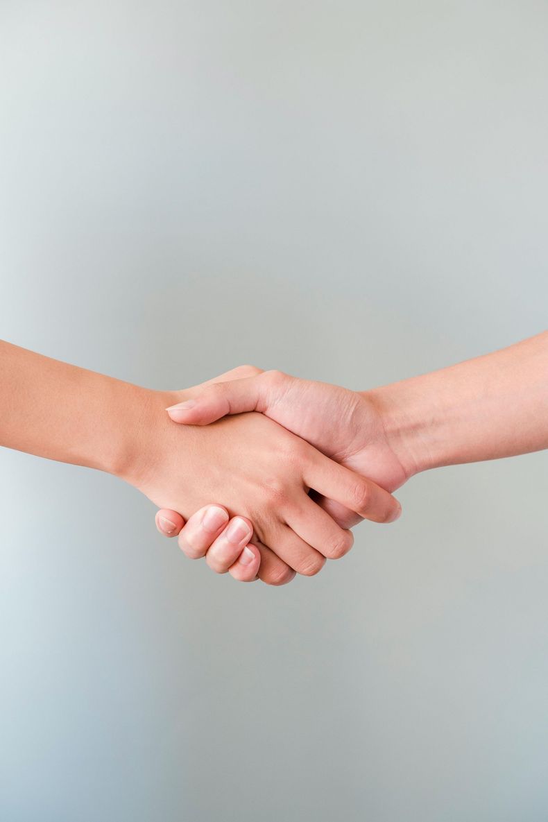 Two men shaking hands, one with dark skin, the other with light skin. They are in a room with dark wood paneling.