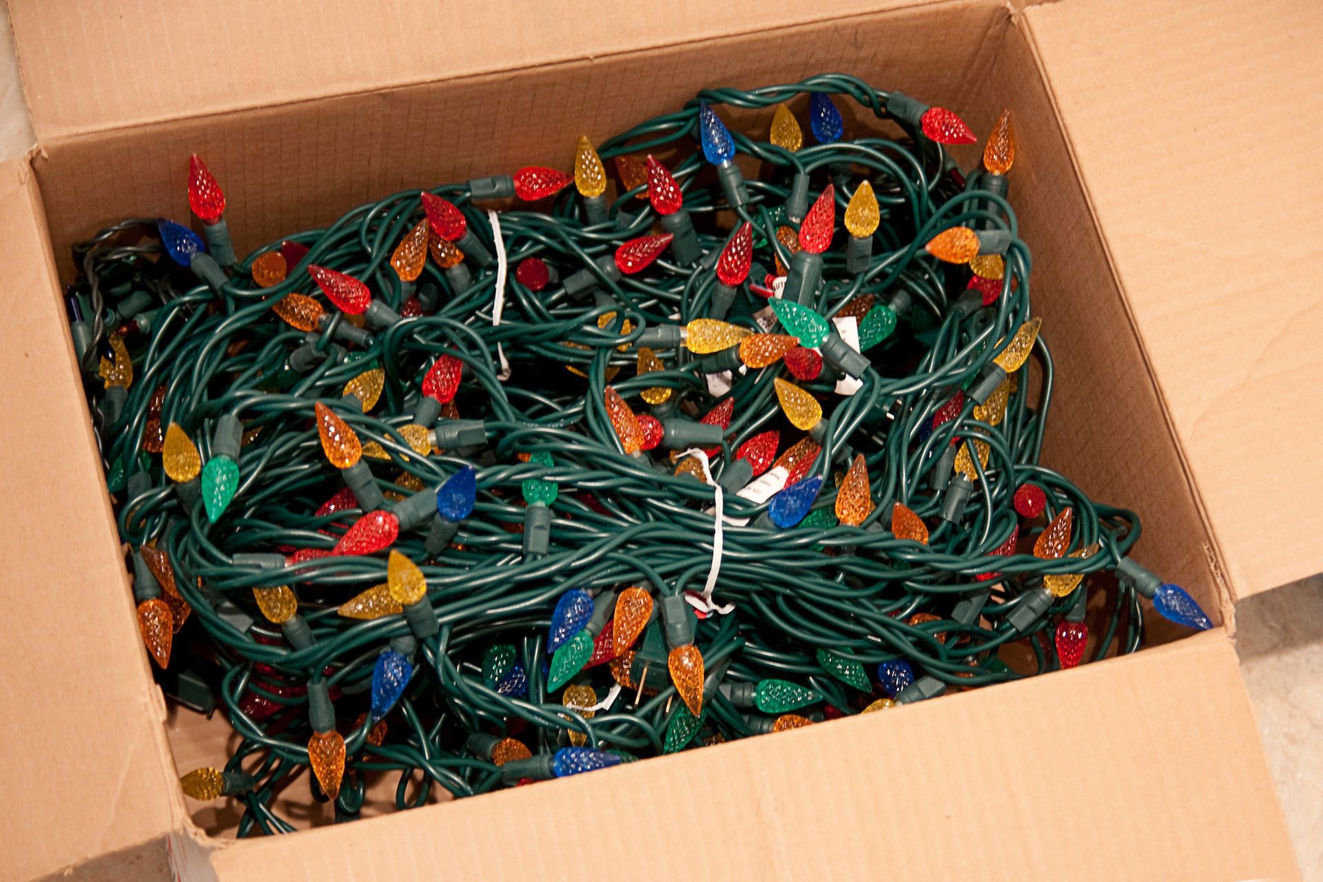 Christmas lights tangled in a cardboard box, with colorful bulbs and green wiring.