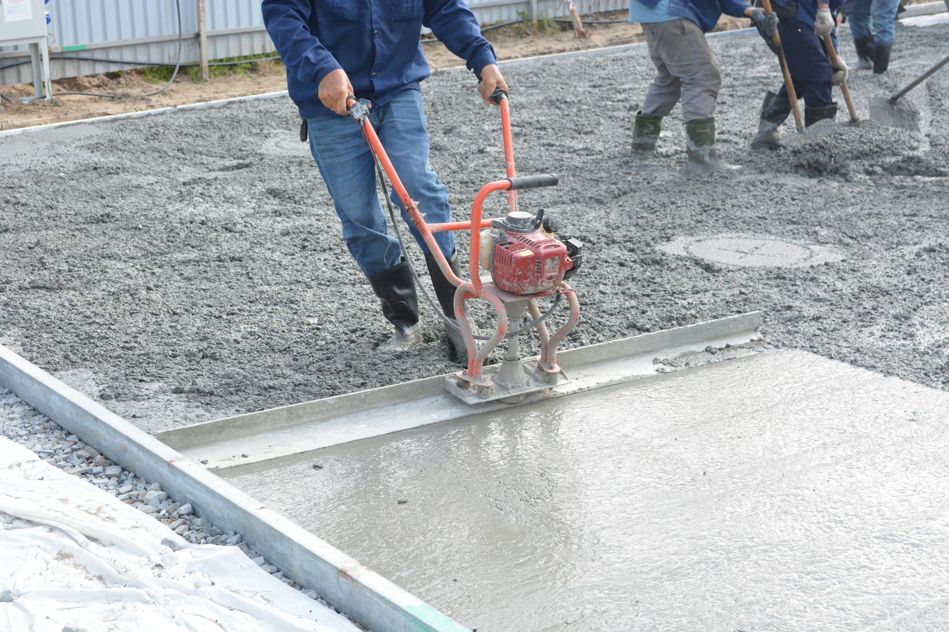 Workers smoothing wet concrete with a power screed on a construction site