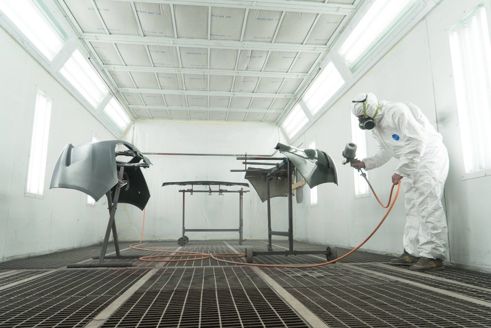 Un uomo sta verniciando un'auto in una cabina di verniciatura.