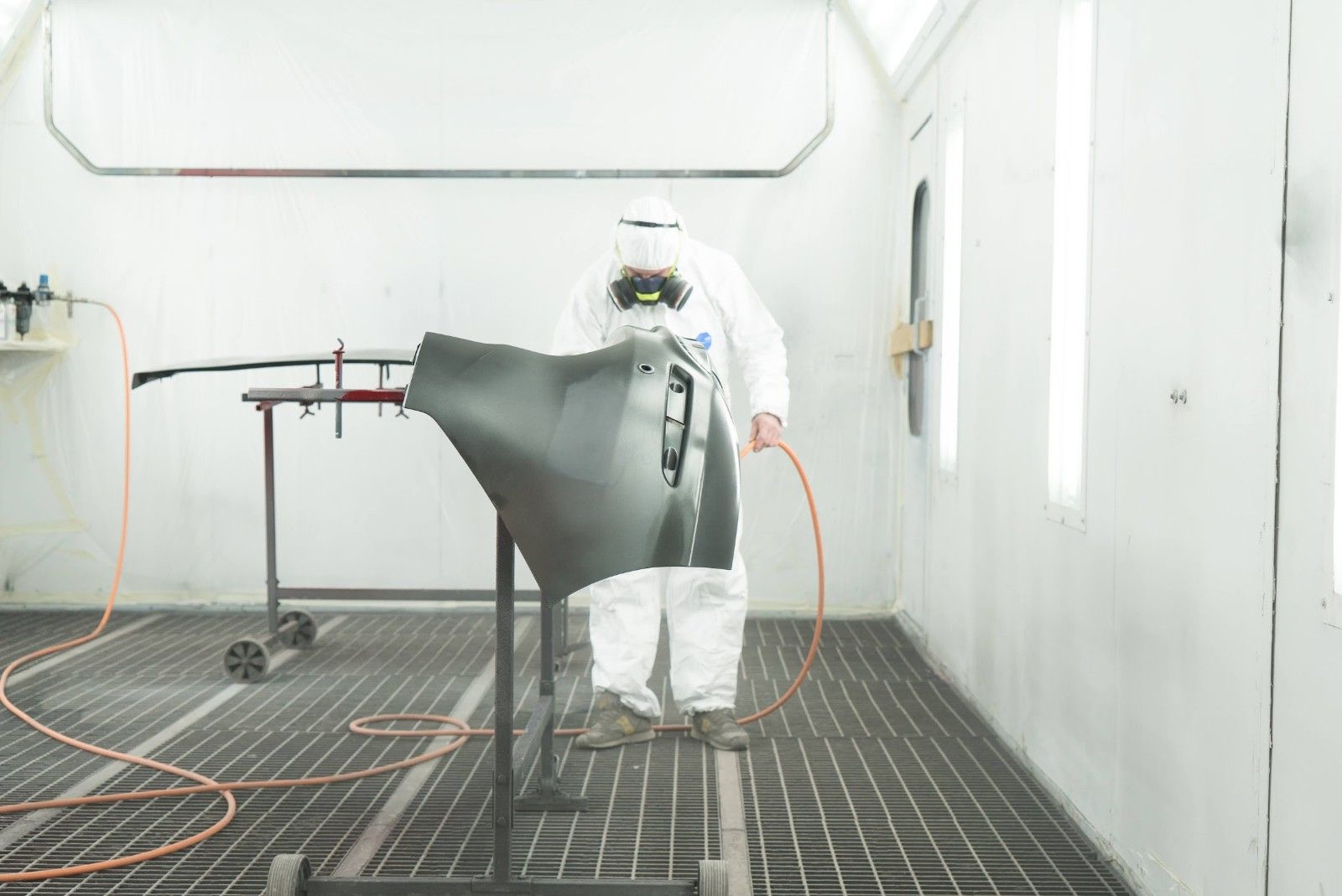 Un uomo con una tuta protettiva sta verniciando un'auto in una cabina di verniciatura.