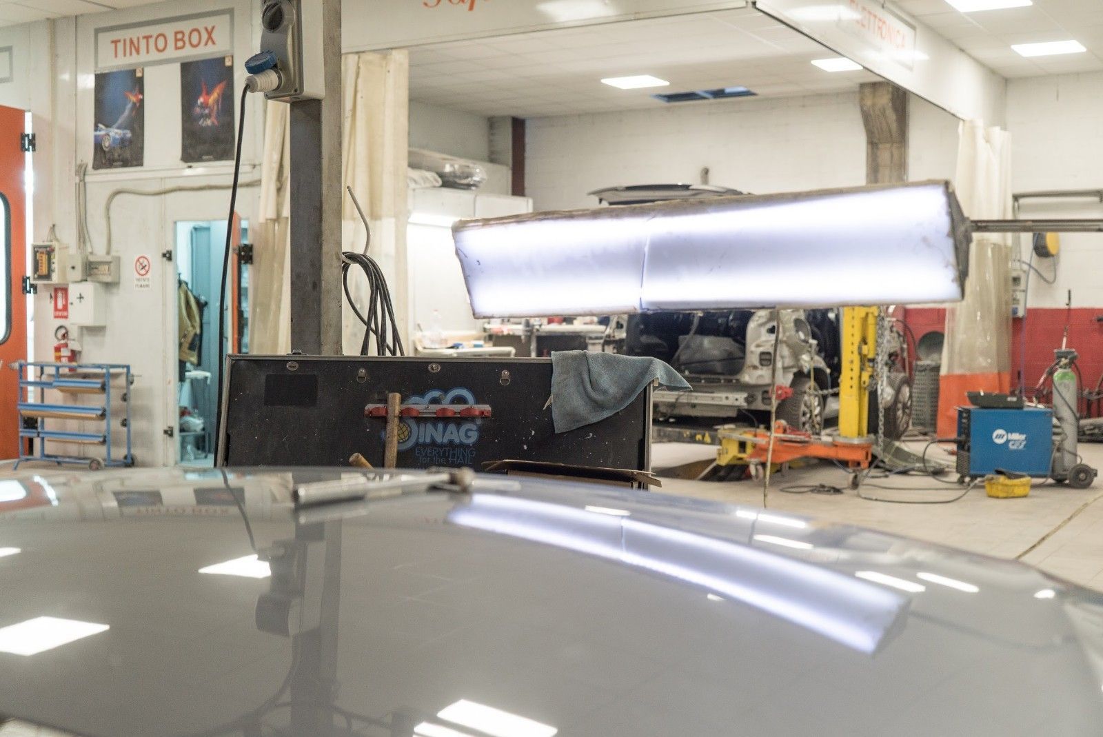 Un'auto viene riparata in un garage con una luce sul cofano.