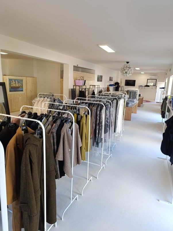 Espositori per abiti in un negozio al dettaglio, con capi in tonalità neutre. Pareti e pavimento bianchi.