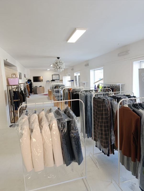 Appendiabiti in uno spazio commerciale bianco e luminoso. Vestiti in sacchetti trasparenti sono appesi agli appendiabiti.