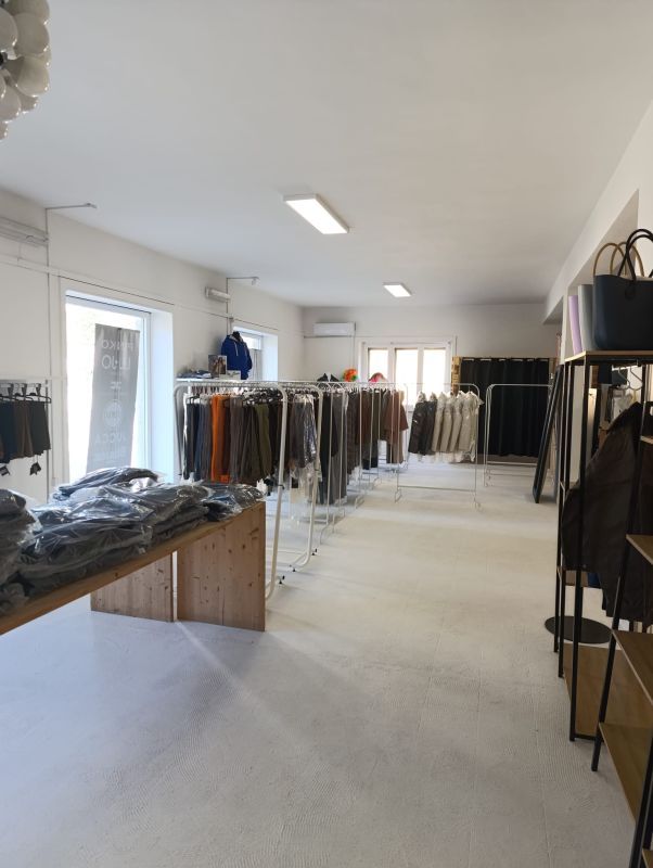 Interno di un negozio di abbigliamento con espositori per abiti e merce esposta su scaffali e rastrelliere in legno.