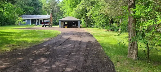 A dirt road leading to a house with a tractor parked in front of it.