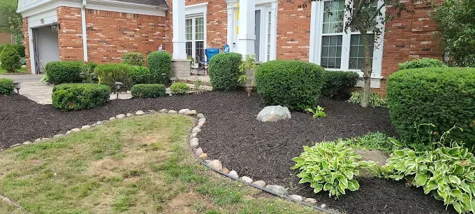 A brick house with a lush green lawn and bushes in front of it.