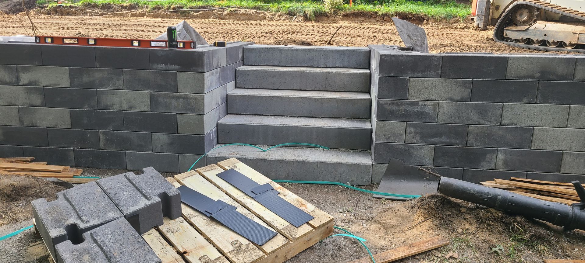 Construction of retaining wall with steps built from gray concrete blocks.