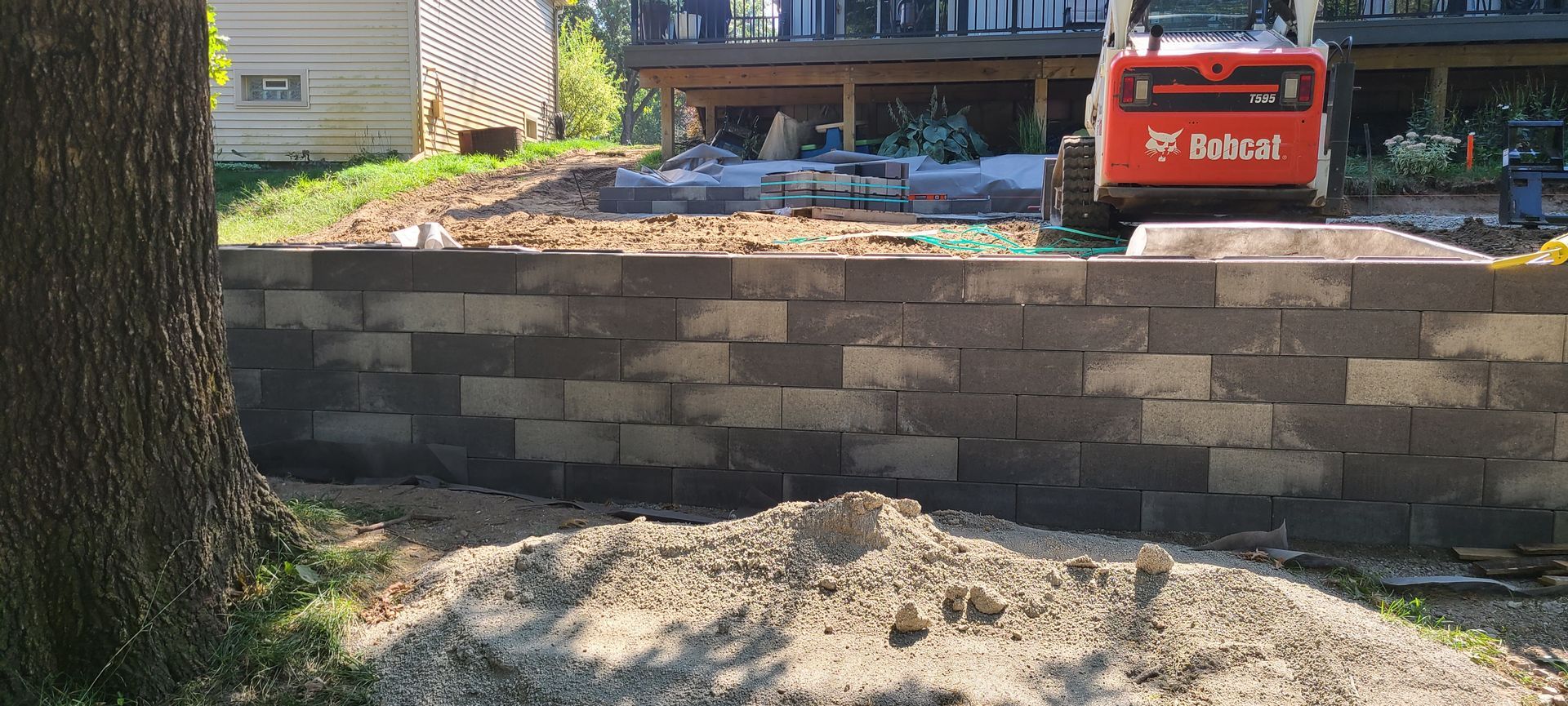 A retaining wall made of concrete blocks, with a Bobcat in the background.