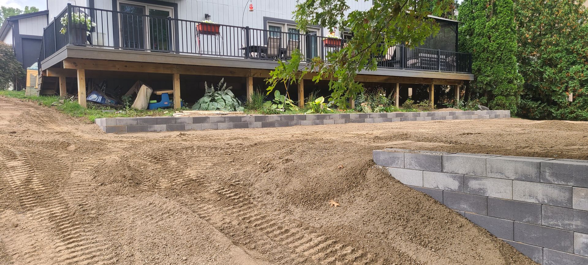 A house with a raised wooden deck and a retaining wall made of gray blocks in a yard.