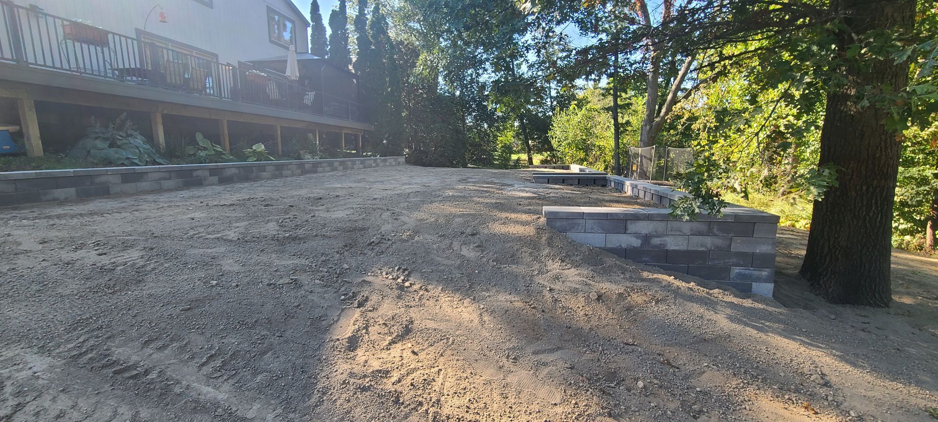 Gravel yard with a house and stacked stone planters. Large tree on the right.