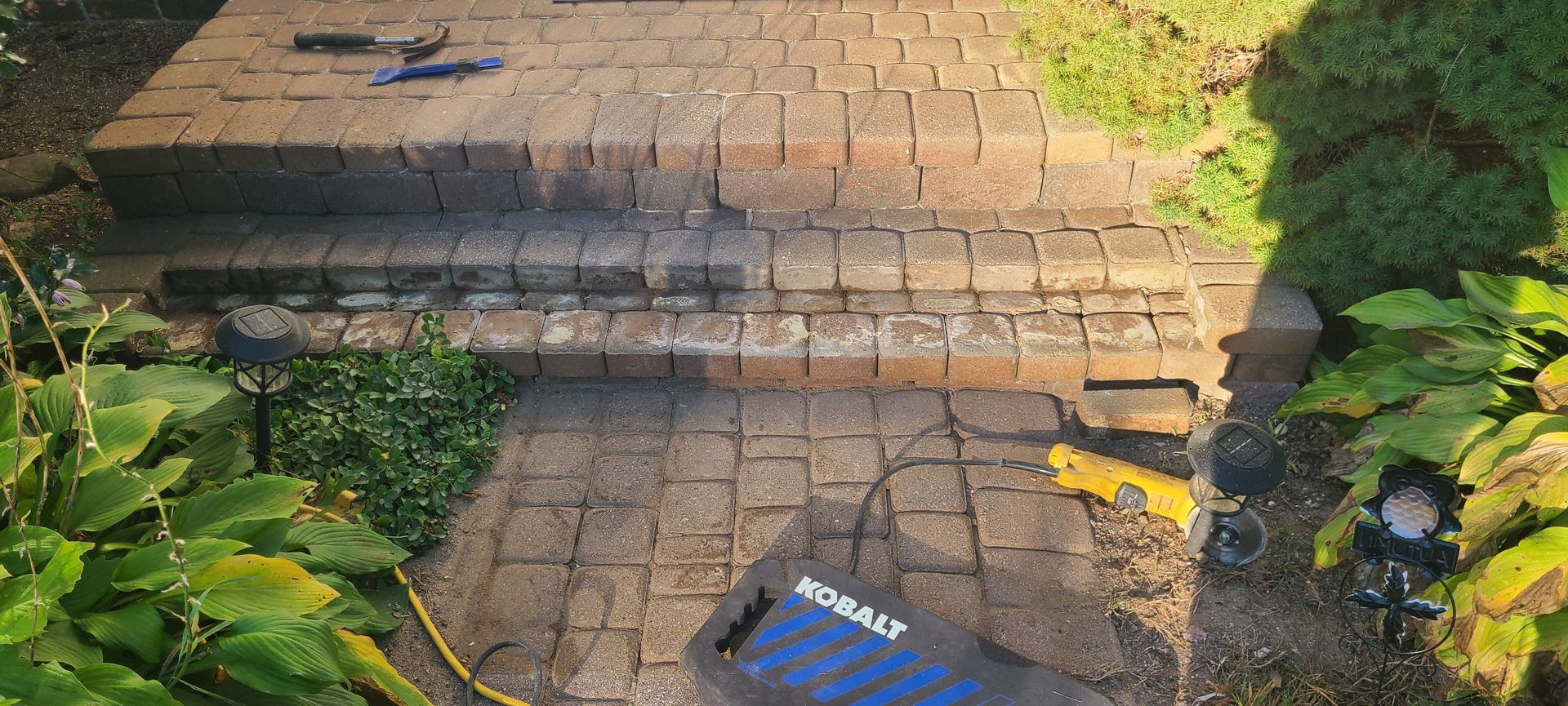 Brick steps with plants on either side and tools on the top step. A blue tool is visible on the bottom step.