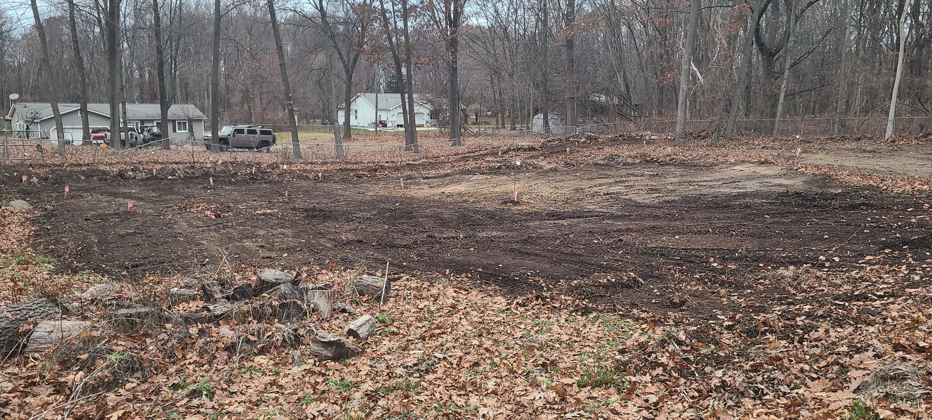 Brown dirt field with bare trees and houses in the distance.